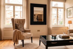 A well-lit room with a large armchair, a coffee table with decorative items, and a mirror on the wall. - Mayfair`s Finest: Modern 2 bedroom apartment! (Greater London)