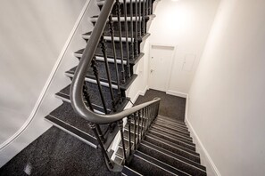A staircase with a handrail, carpeted steps, and a white door at the bottom. - Mayfair`s Finest: Modern 2 bedroom apartment! (Greater London)