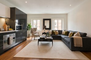 Ein modernes Wohnzimmer mit einem dunkelgrauen Sofa, einem Couchtisch und einer Küchenzeile inklusive Herd und Backofen.