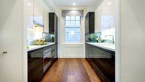 Una cocina estrecha con piso de madera, muebles blancos y una ventana con vistas.