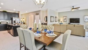 A modern kitchen with dark cabinets, a central island, and a dining area with a wooden table set for four. - Fs14327ha - Champions Gate Resort - 6 Bed 5 Baths Villa (Davenport)