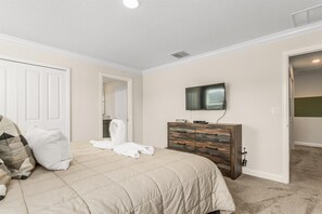 A bedroom with a bed, a dresser, a television, and a door leading to another room.