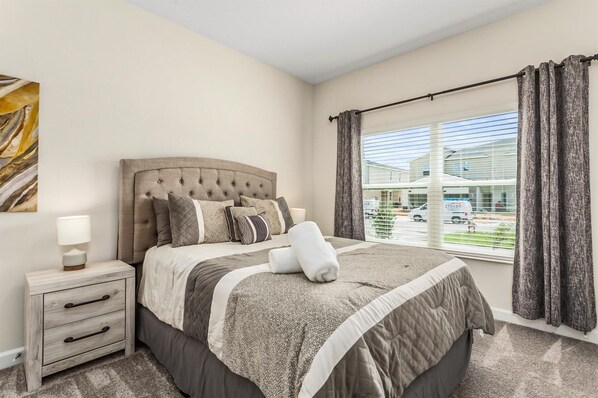 A bedroom with a large bed, a bedside table, a lamp, and a window with curtains.