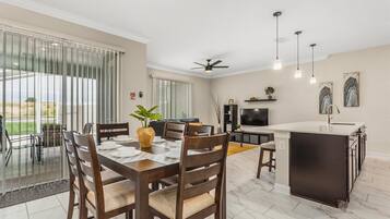 A spacious kitchen with a dining area, large windows, and a ceiling fan.
