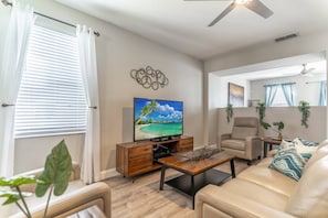 A living room with a TV, a sofa, a coffee table, and a chair. There are plants and a ceiling fan. - It11484ha - Windwood Bay - 5 Bed 4 Baths Villa (Davenport)