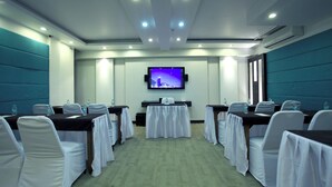 Un salón de conferencias con mesas, sillas, una pantalla de televisión y un equipo de aire acondicionado.