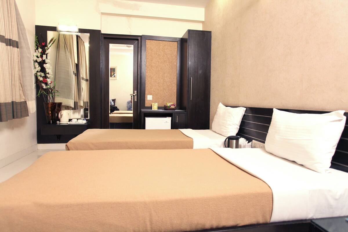 Une chambre d’hôtel avec deux lits, un grand miroir, une coiffeuse avec un lavabo et une petite table sur laquelle est posé un vase de fleurs.