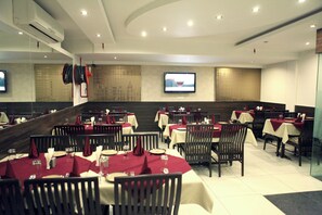 A restaurant with multiple tables set for dining, a flat-screen TV mounted on the wall, and an air conditioning unit on the ceiling. - Hotel Saar Inn (New Delhi)
