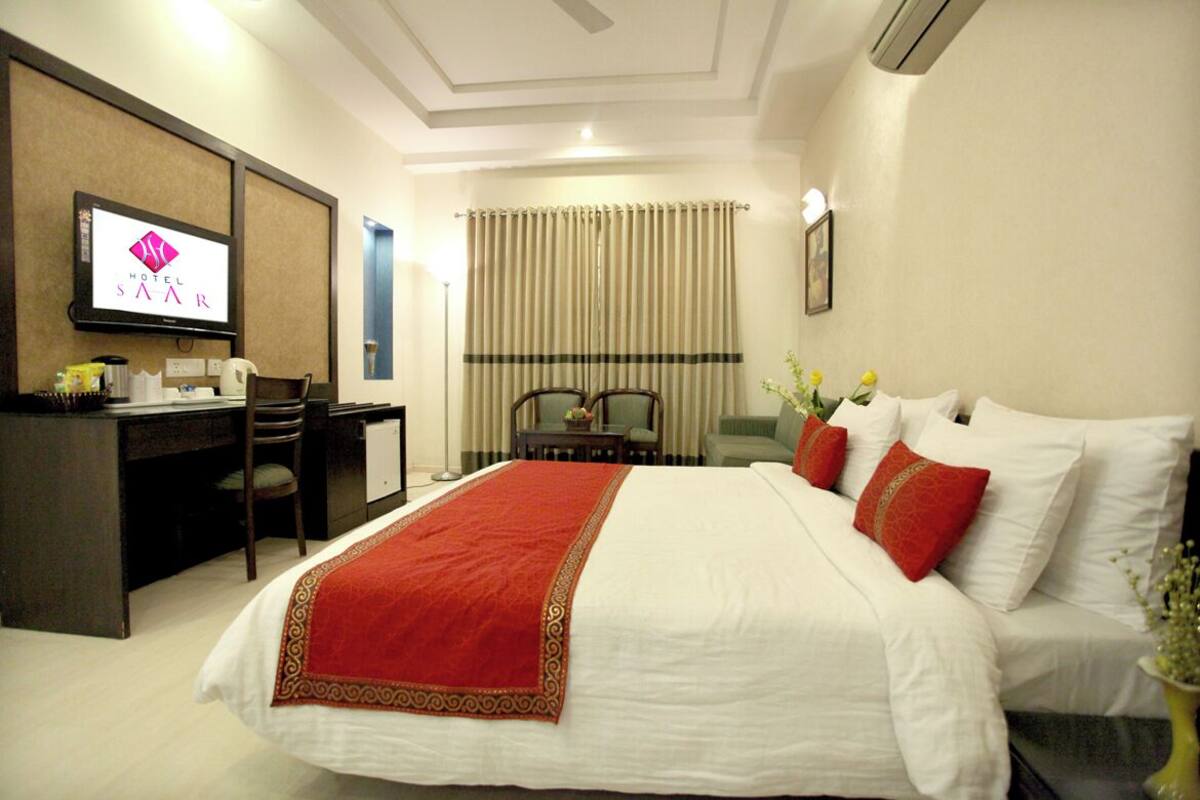 Une chambre d’hôtel équipée d’un lit, d’un bureau, d’une chaise et d’un téléviseur affichant le logo de l’hôtel.