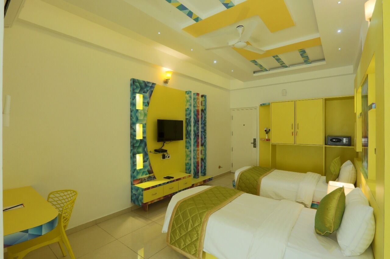 A hotel room with two beds, a TV, a desk, and yellow cabinets.