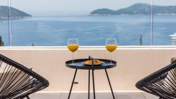 Un balcon avec une table et deux chaises, une assiette de nourriture et deux verres de jus d’orange.