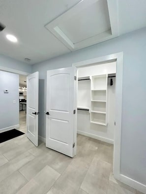 Ein Flur mit zwei weißen Türen, einem eingebauten Kleiderschrank mit Regalen und einer Küche im Hintergrund.