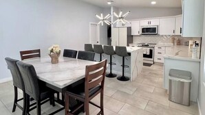 A modern kitchen with white cabinets, a central island, and a dining area with a marble table and chairs.