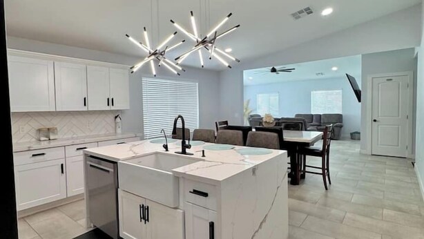 A modern kitchen with white cabinets, a marble island, and pendant lighting.