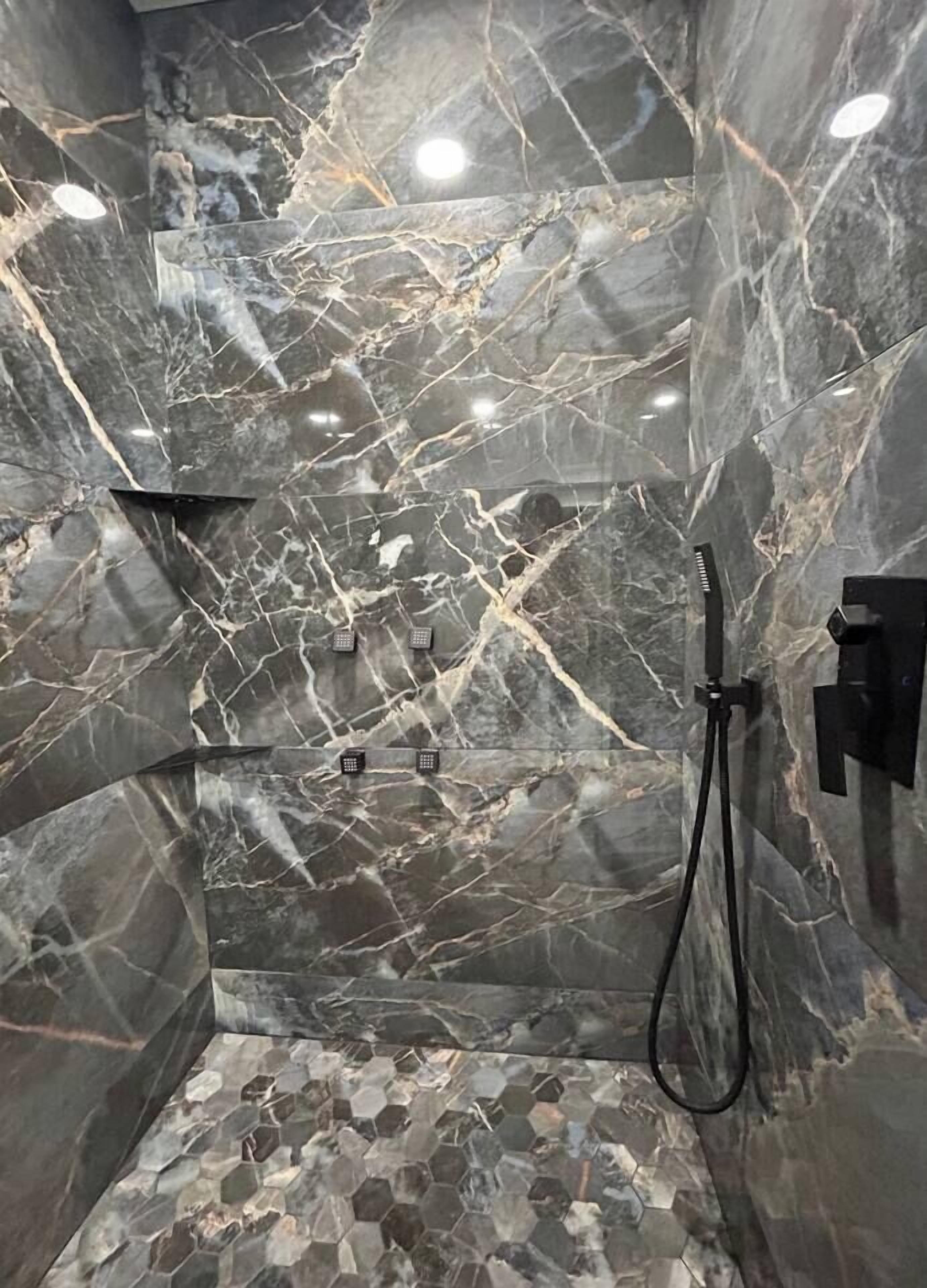 Una ducha con paredes de mármol y suelo de baldosas hexagonales.