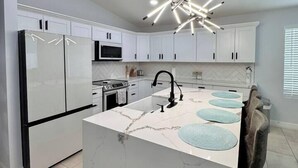 A modern kitchen with white cabinets, a marble island, a black refrigerator, and a unique ceiling light fixture.