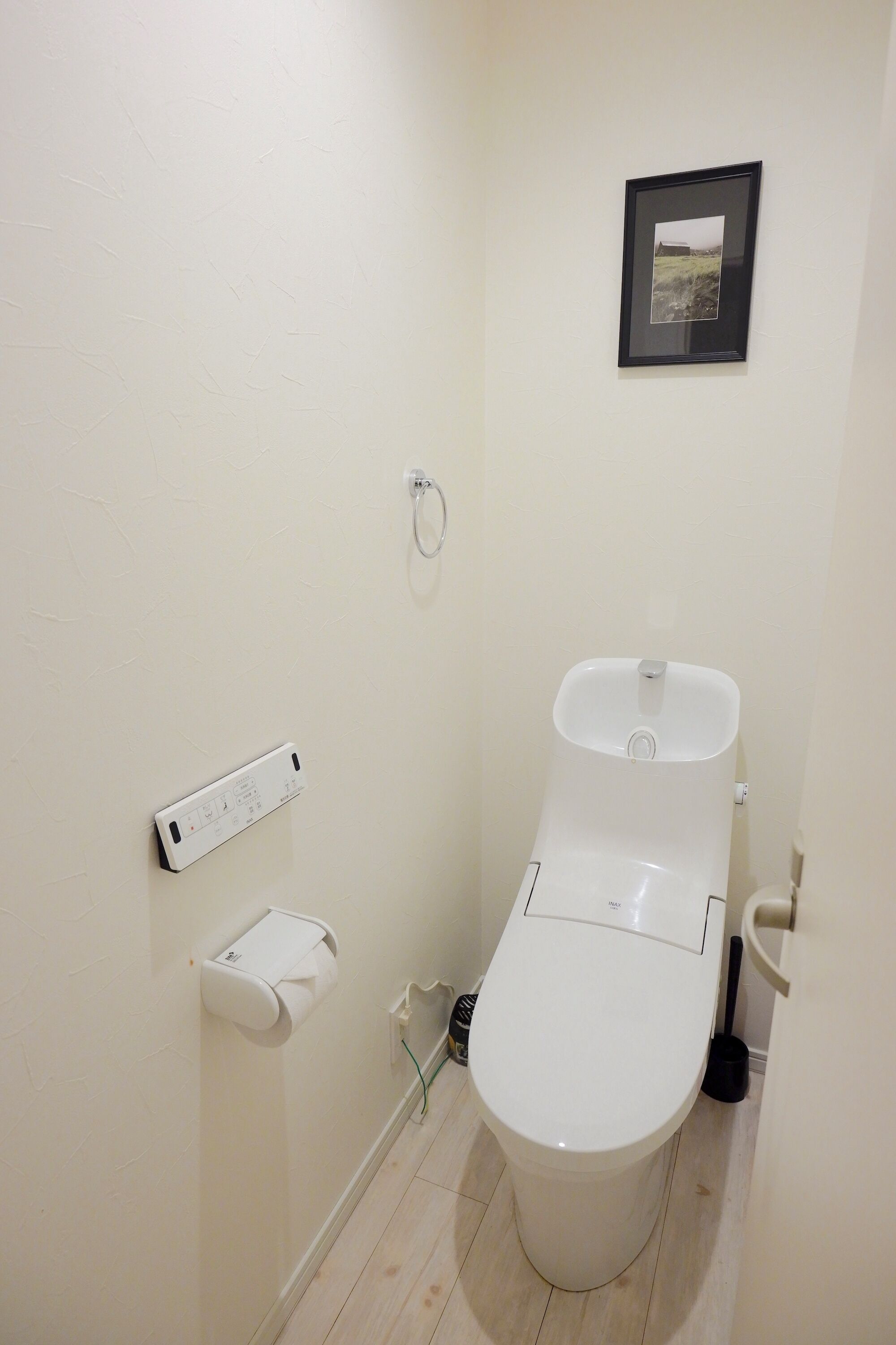 A small, clean bathroom with a toilet, a paper towel dispenser, and a picture on the wall.