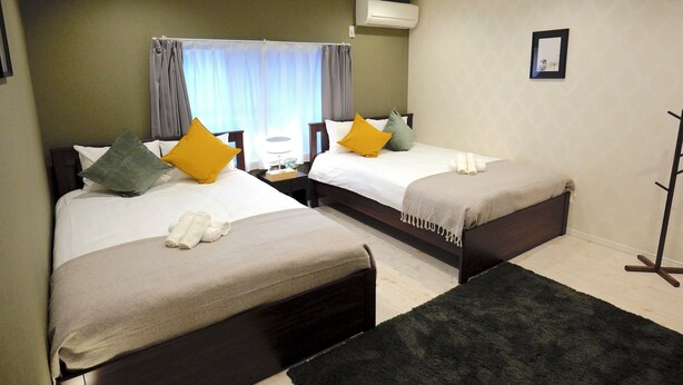 Habitación de hotel con dos camas, una mesita de noche, aire acondicionado, un espejo y una alfombra negra.