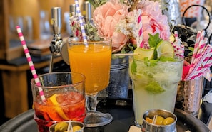 Trois boissons servies avec des pailles, un récipient en métal contenant des fleurs et un plateau en métal.