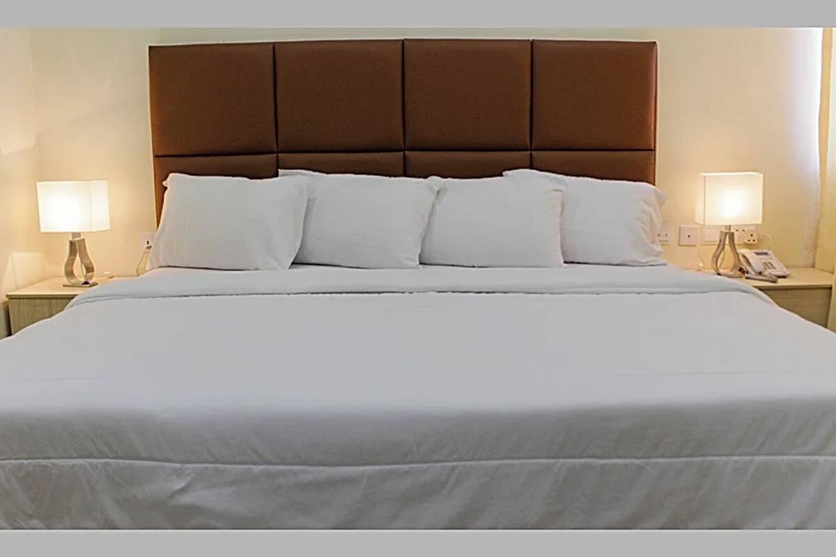 A neatly made bed with a brown headboard, white bedding, and two bedside lamps on either side.