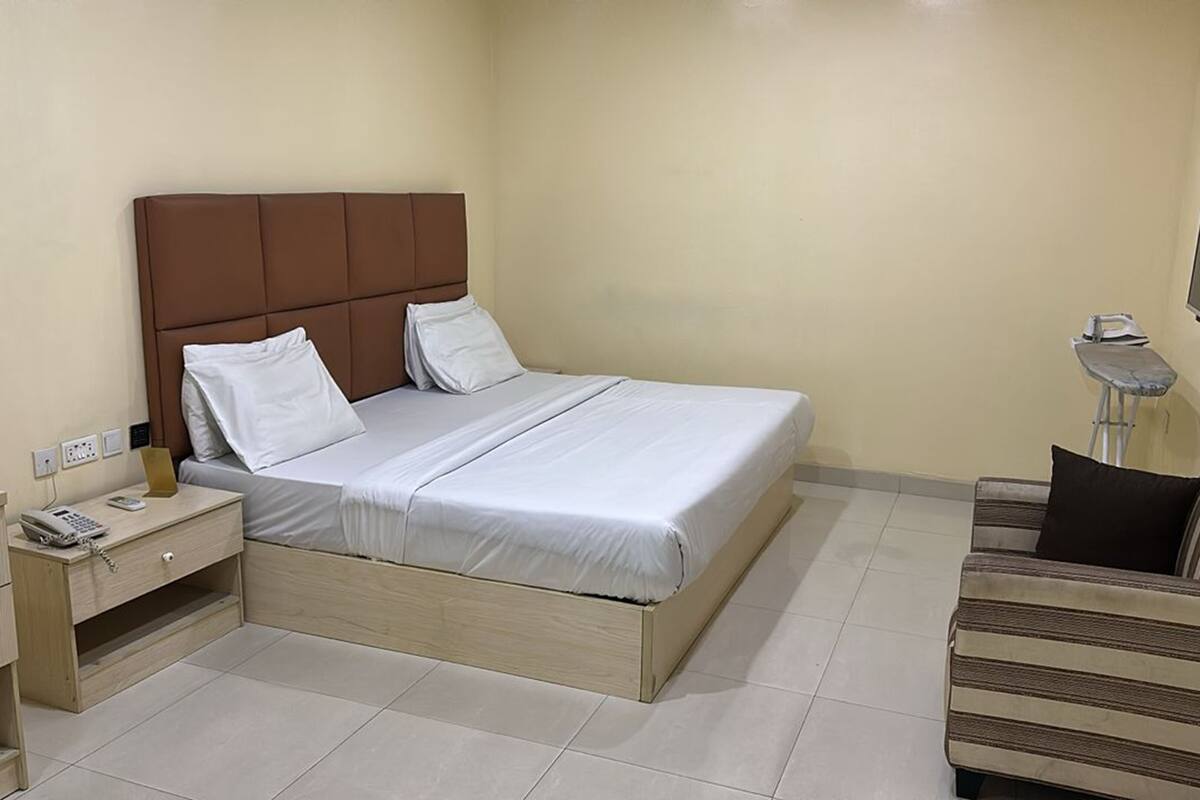 A hotel room with a bed, bedside table, lamp, and a small sofa.