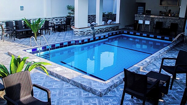 Zona de piscina con suelo de baldosas, sillas de descanso y un área de bar.