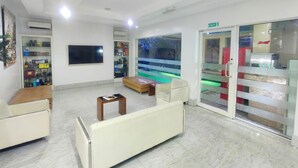 Un vestíbulo amplio con área de descanso, un televisor montado en la pared y una puerta de cristal que da al exterior.