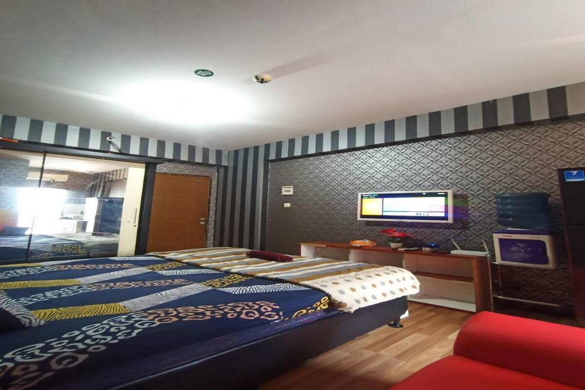 A hotel room with a bed, a red chair, a TV, and a desk with a computer.