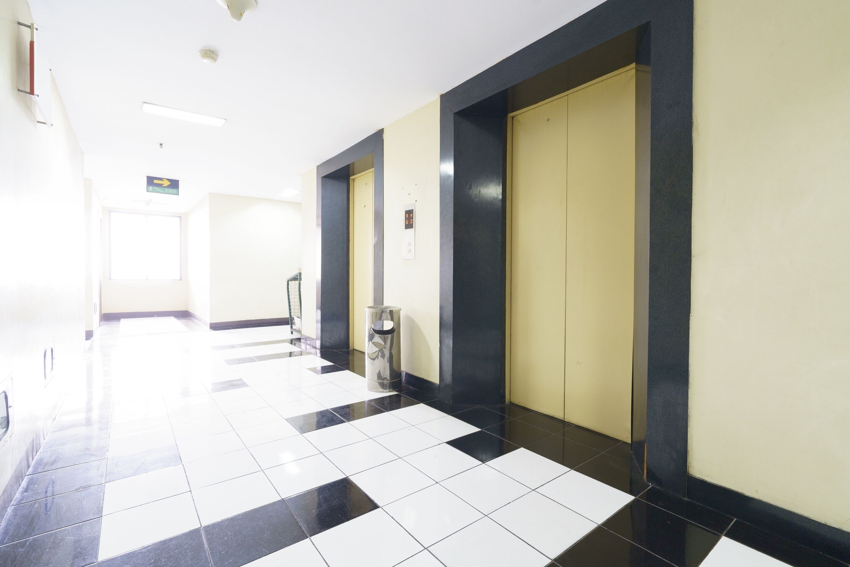 A hallway with a checkered floor, doors, and a trash bin.