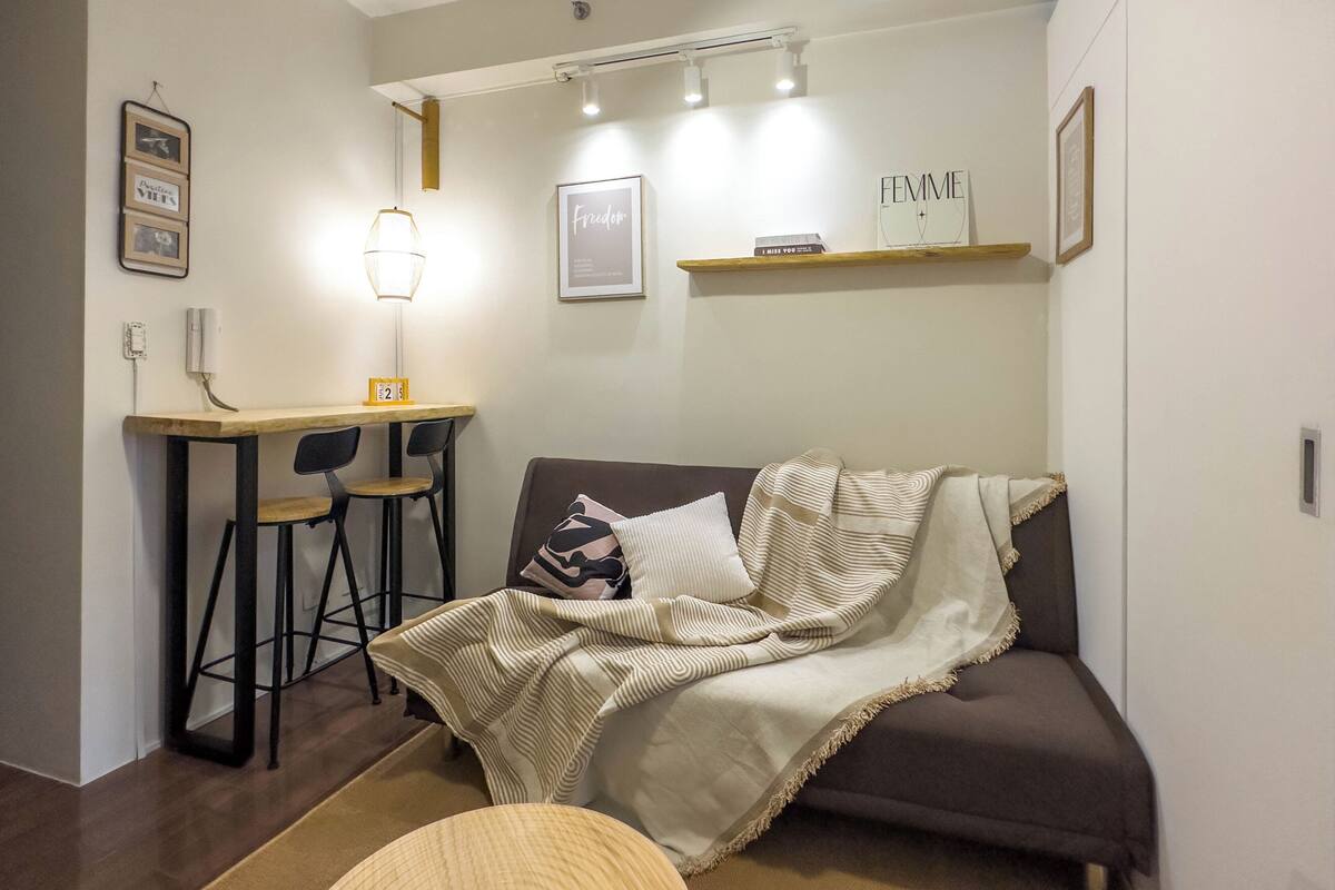 Un espacio habitable pequeño y acogedor con un sofá, una mesita con sillas y una estantería llena de libros.