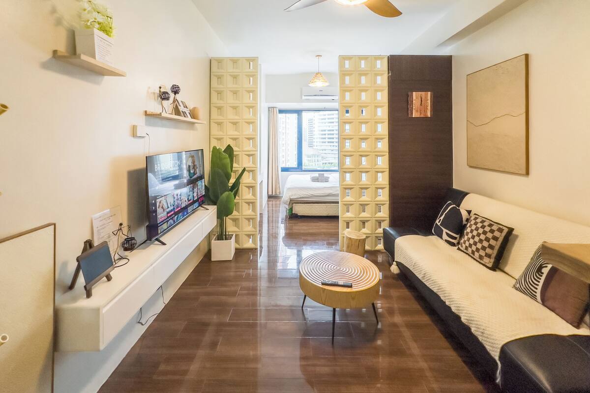 Una sala de estar moderna con un televisor de pantalla plana, un sofá, una mesa de centro y una planta decorativa.