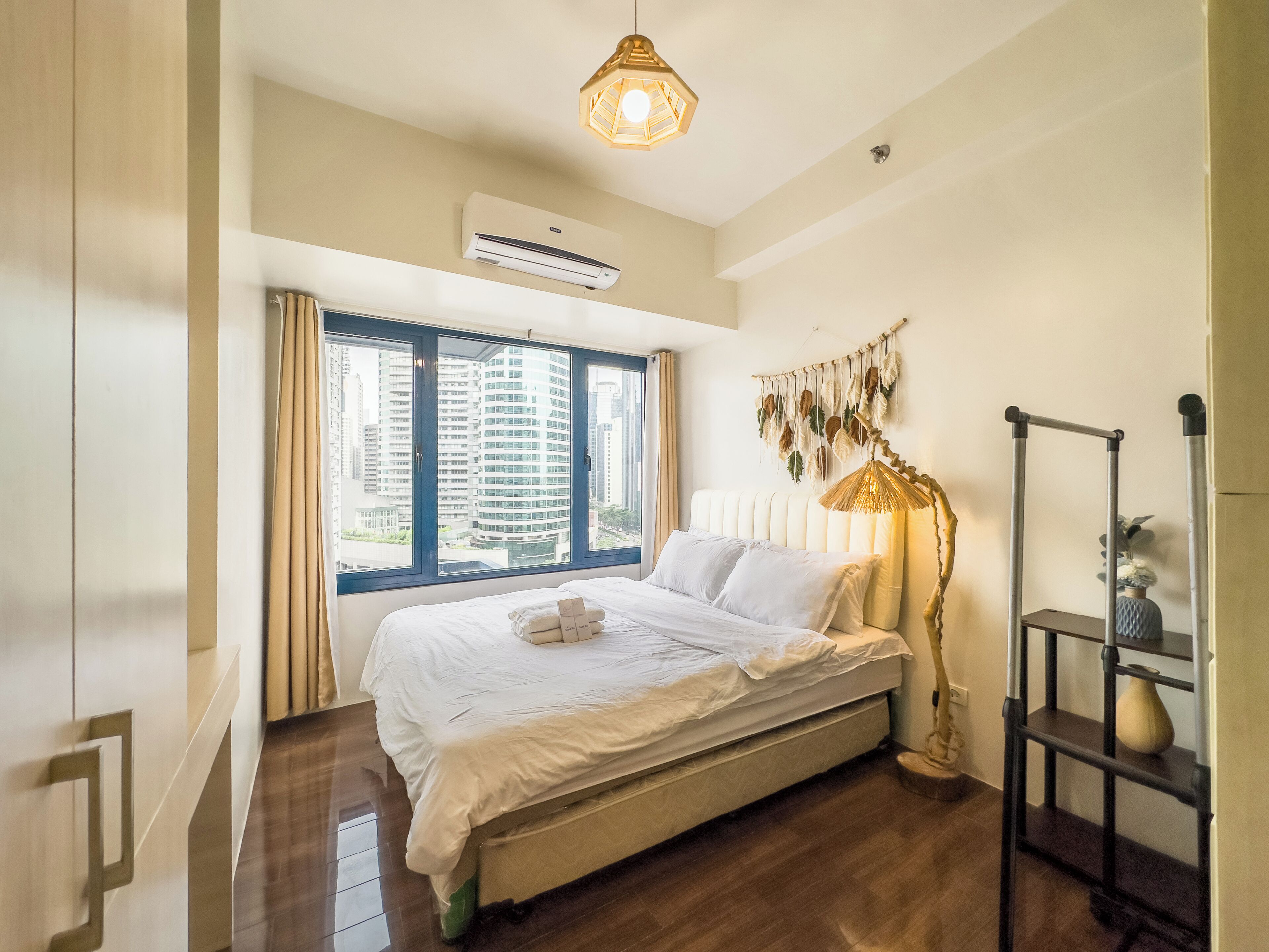 A bedroom with a large bed, a window with curtains, a wall-mounted air conditioner, and a floor lamp.
