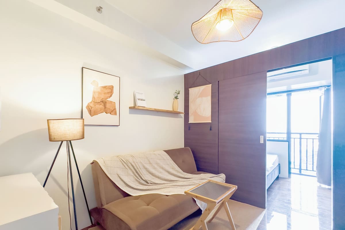 Una sala de estar moderna con un sofá, una pequeña mesa de madera, una lámpara de pie y obras de arte en las paredes.