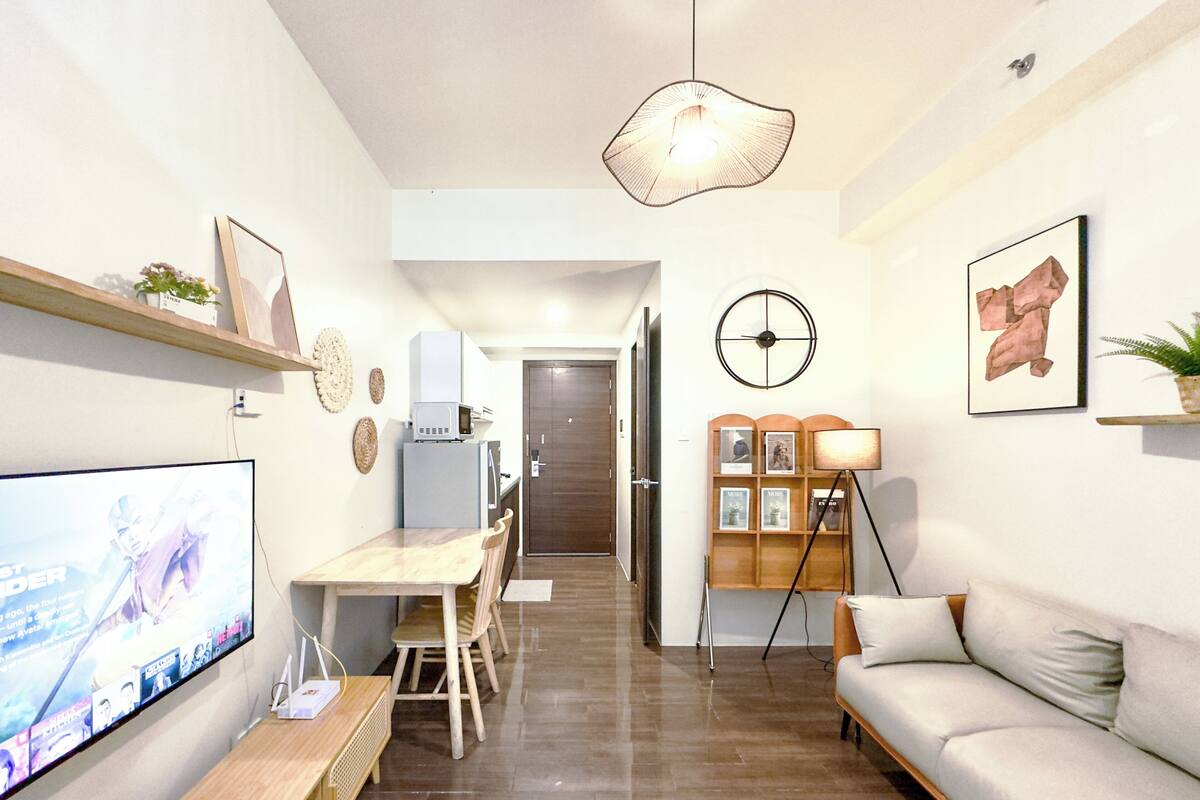 Una sala de estar moderna con una televisión de pantalla plana, una mesa de comedor de madera, un sofá y una cocina con microondas y refrigerador.