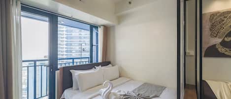 Une chambre d’hôtel moderne dotée d’un grand lit, offrant une vue sur la ville grâce à de larges fenêtres du sol au plafond, et d’un climatiseur fixé au plafond.