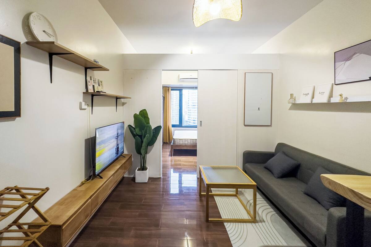 Una sala de estar moderna con una televisión de pantalla plana, un sofá, una mesa de centro y una lámpara colgante.