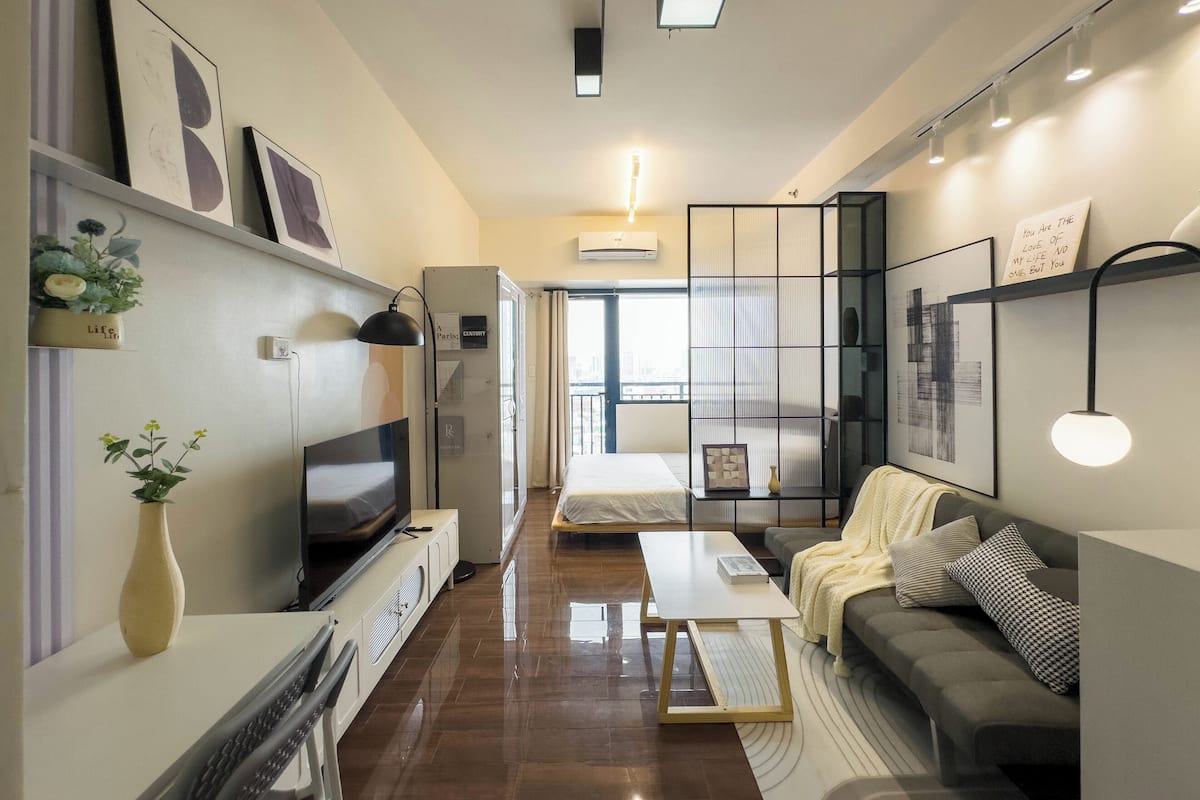 Una habitación de hotel moderna con cama, sofá, televisión y un ventanal grande.