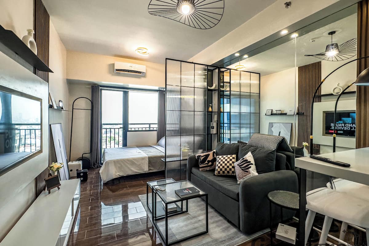 Una habitación de hotel moderna con cama, sofá, una mesita y un espejo. Se ve una ventana con vistas a la ciudad.