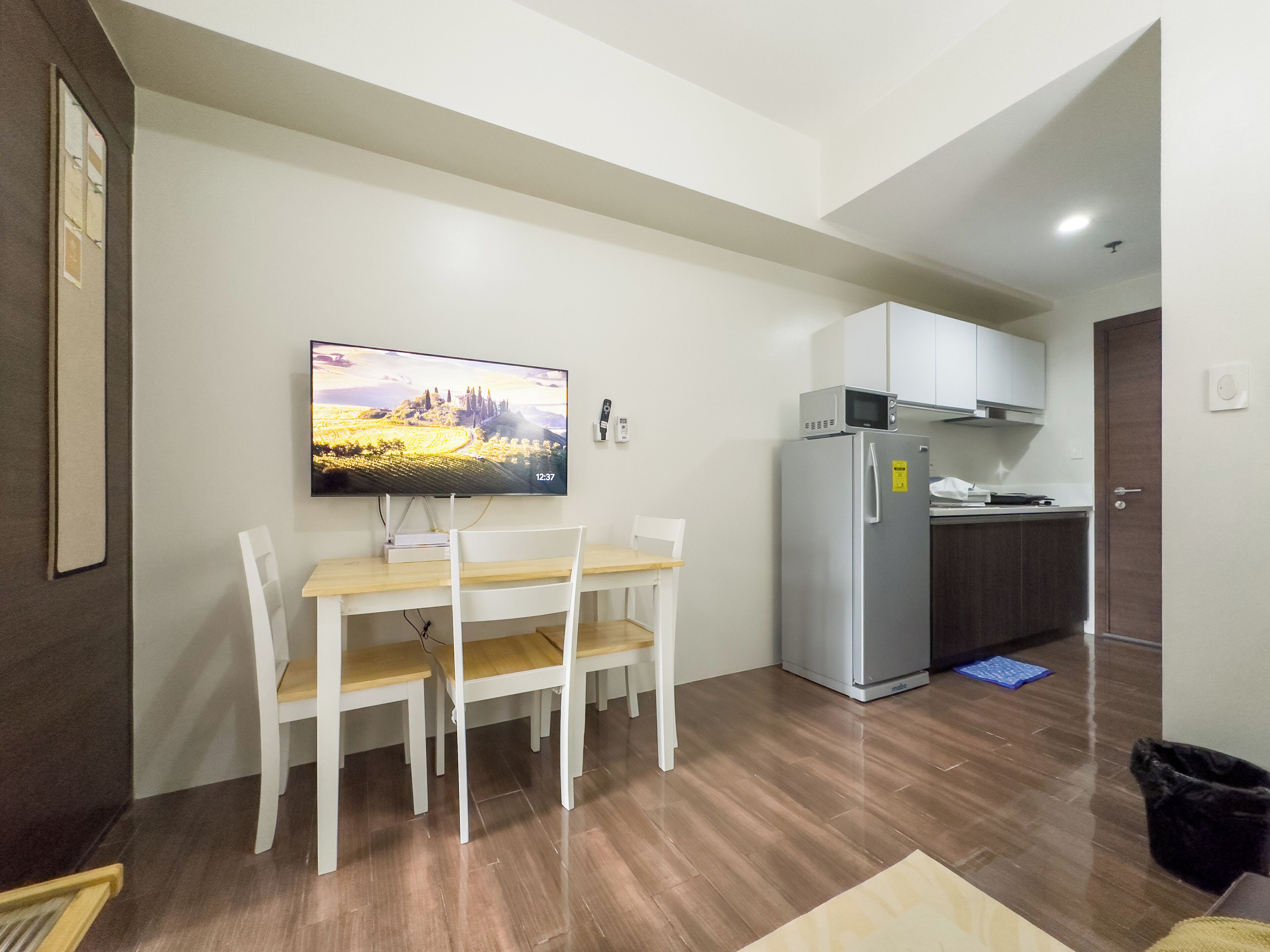 A modern kitchen with a refrigerator, microwave, and a flat-screen TV mounted on the wall.