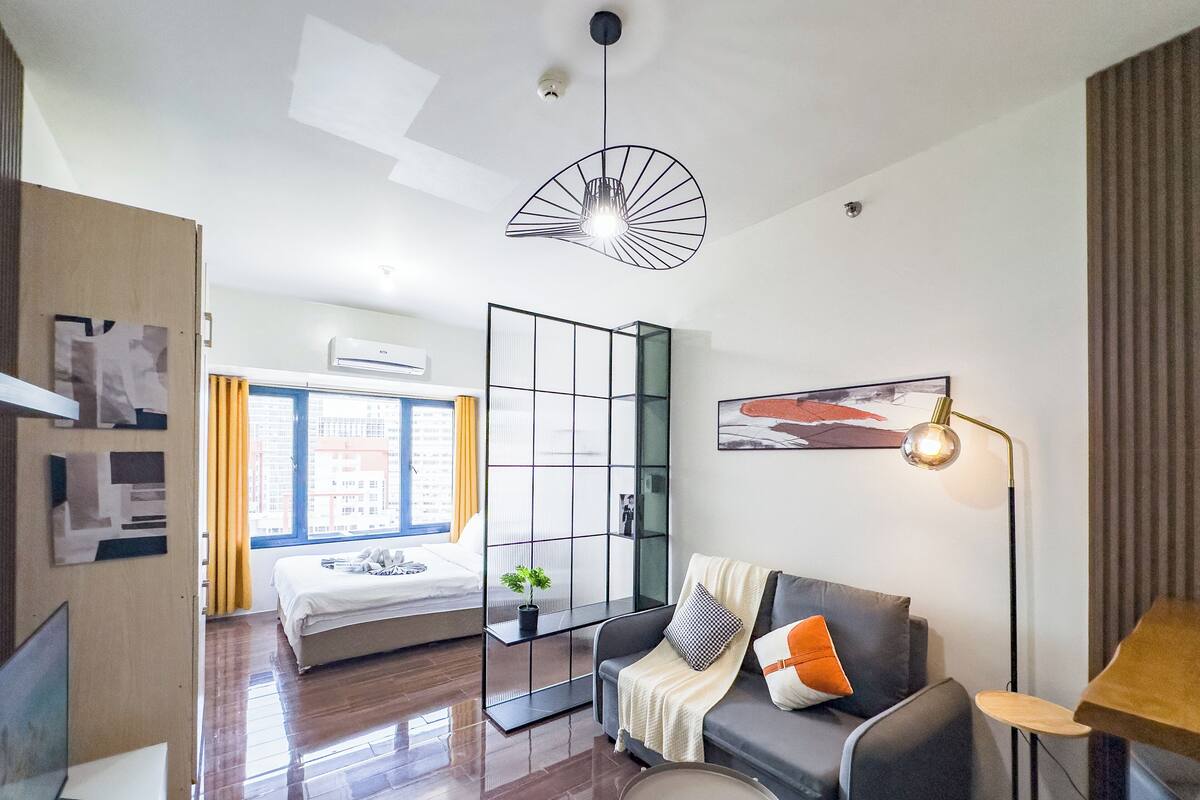 Una habitación de hotel moderna con una cama, un sofá, una mesita y una lámpara de pie.
