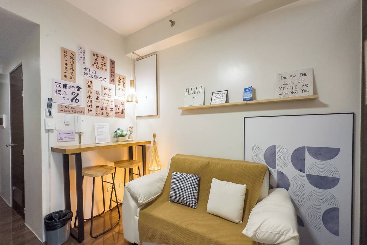 Una habitación moderna y bien iluminada con un sofá blanco, una mesita pequeña y una pared decorada con diversos objetos y notas enmarcadas.