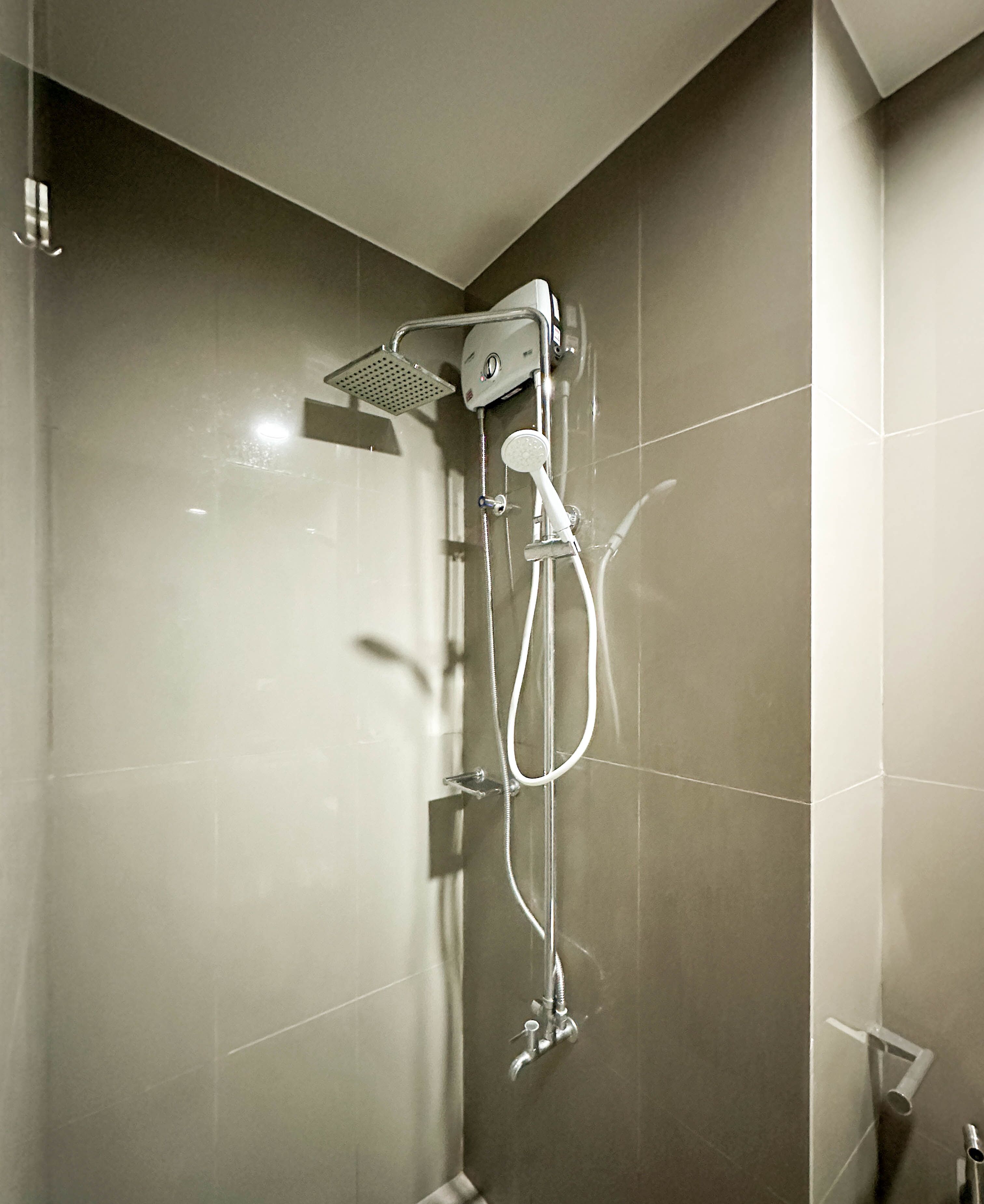 Une douche moderne équipée d’un pommeau de douche à main et d’un pommeau de douche fixe, tous deux fixés sur un mur recouvert de carreaux brillants.