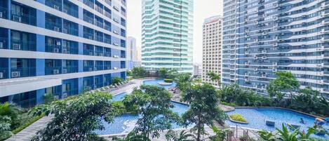 A modern residential complex with multiple high-rise buildings, a central swimming pool, and surrounding greenery.