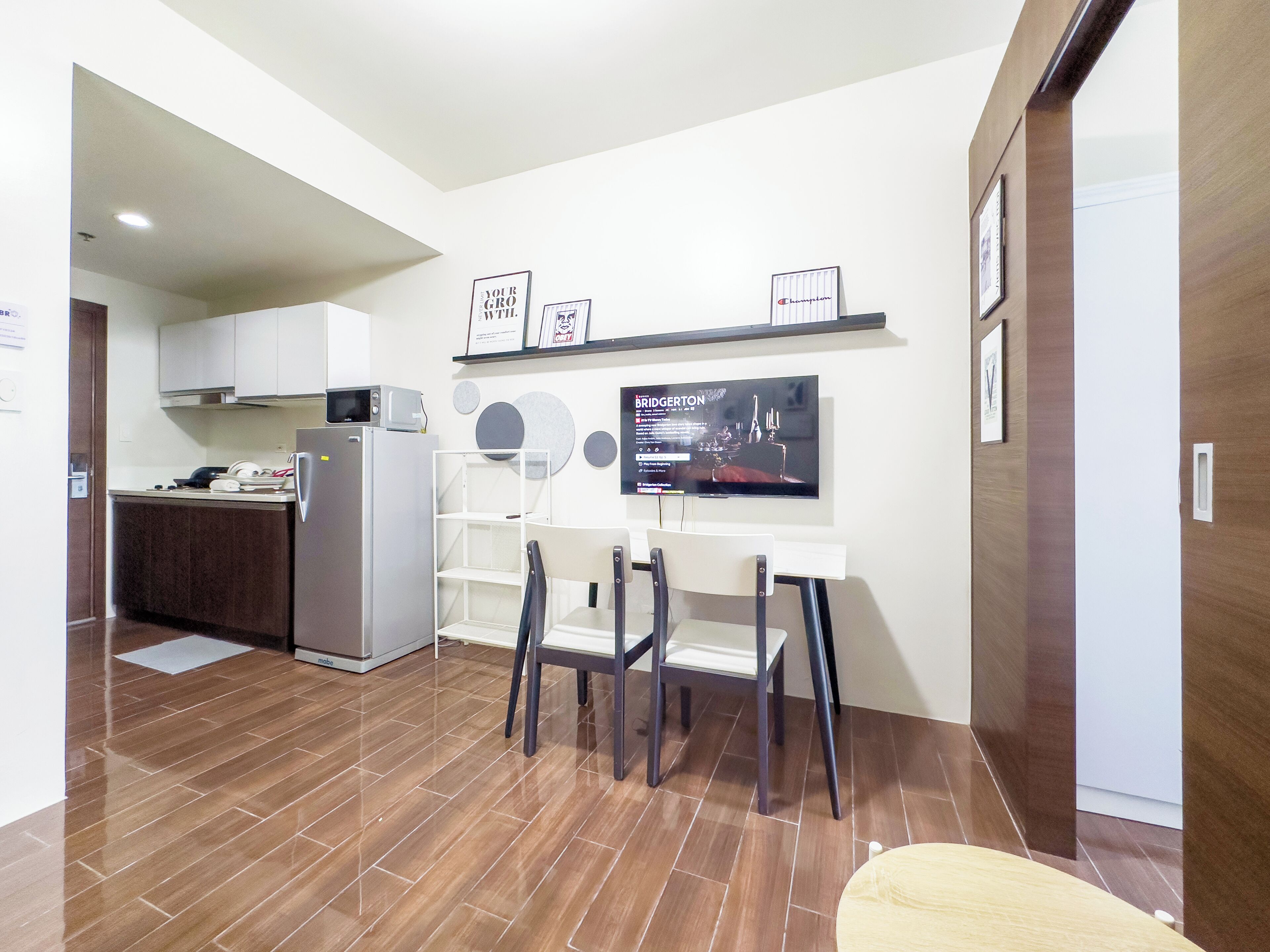 Una cocina moderna con refrigerador, microondas y un comedor con televisión mostrando un programa.
