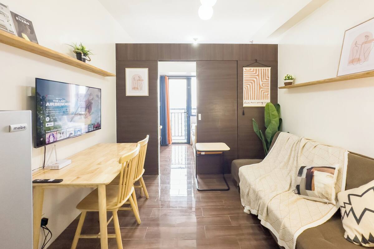 Una sala de estar moderna con televisión, muebles de madera, un sofá y una zona de comedor.