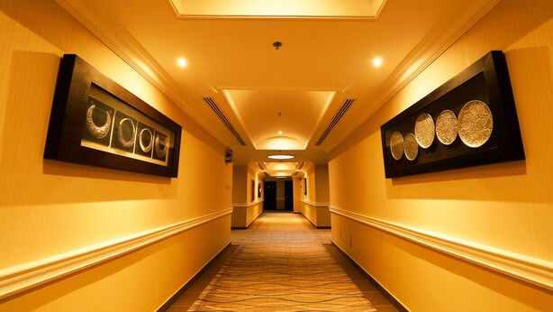 A hotel hallway with a carpeted floor, framed artwork on the walls, and a ceiling with recessed lighting. - City Residence (Dammam)