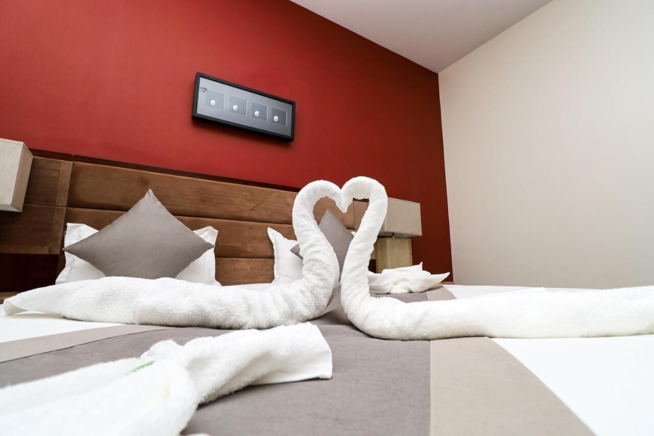 Habitación de hotel con cama, almohadas, cabecero y un interruptor de luz en la pared.