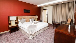 A hotel room with a large bed, a wooden desk, a nightstand, and a chair. - City Residence (Dammam)