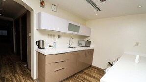 A modern kitchen with wooden flooring, white cabinets, a microwave, and a kettle. - City Residence (Dammam)