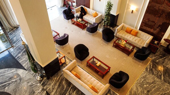 A spacious lobby with a marble floor, multiple seating areas including sofas and armchairs, and a large potted plant.